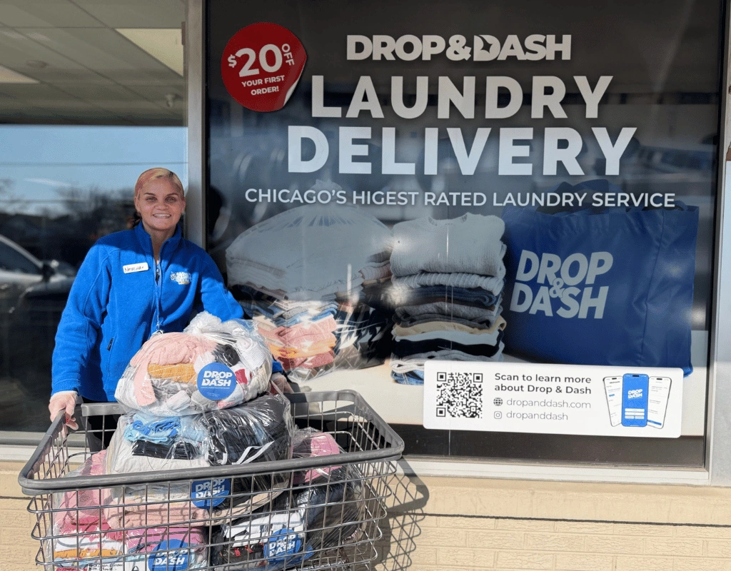 Employee pushing a cart of wrapped laundry past a storefront window advertising $20 off laundry delivery
