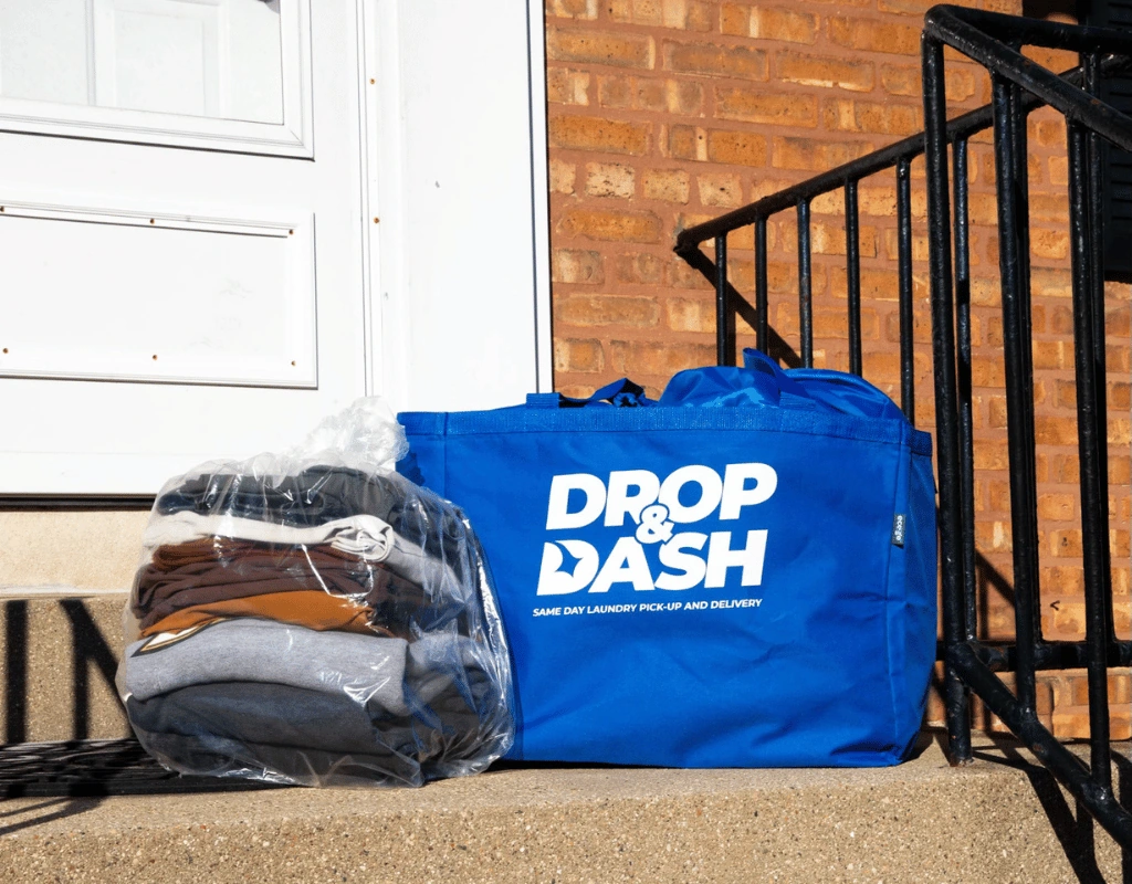 Blue Drop & Dash tote and a sealed bundle of folded laundry sitting on a front stoop beside a black railing