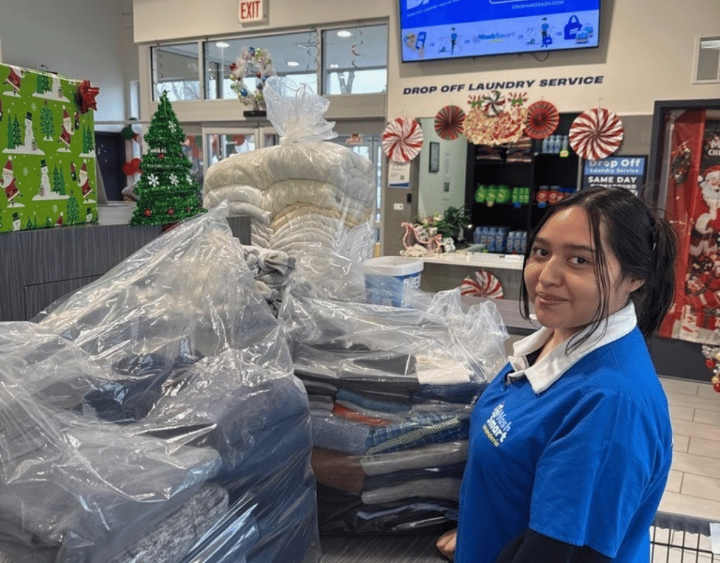 Employee in a blue shirt standing beside large plastic-wrapped bundles of folded laundry near a drop-off counter