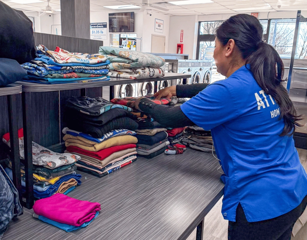 Attendant in a blue shirt folding clothing at a counter with sorted stacks of garments in front of her