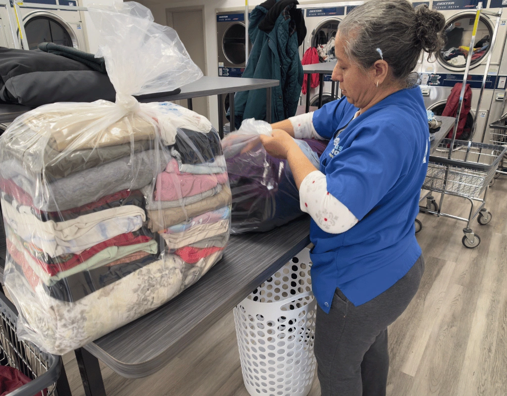 Employee in a blue shirt sealing a plastic-wrapped stack of folded towels and clothing at a folding table